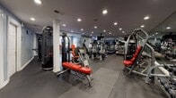 The fitness center at 500 Bedford St in Stamford, Connecticut is a comprehensively outfitted facility designed to support a full range of workout routines. The single-floor space features a dark rubberized flooring throughout, providing a durable and functional surface suited to high-traffic exercise use. Recessed ceiling lighting illuminates the entire area evenly, creating a bright and energizing atmosphere.

The cardio zone is well-stocked with multiple Life Fitness treadmills arranged in a row, complemented by elliptical trainers, stair climbers, and an Echelon spin bike. Wall-mounted televisions are positioned throughout the space, including near the treadmill bank, allowing members to stay entertained during cardio sessions. Floor-to-ceiling mirrors line several walls, enhancing the sense of openness and allowing users to monitor their form.

The strength training section offers a diverse selection of resistance machines, including cable systems, chest press, leg press, and seated row equipment, many featuring distinctive red upholstered seating. Free weight options and medicine balls are also available. A Matrix cable tower adds further versatility to the strength training offerings.

The facility also benefits from natural light provided by windows fitted with white plantation shutters, adding a touch of comfort to the workout environment. The overall layout is organized and spacious, making for an efficient and motivating fitness experience.