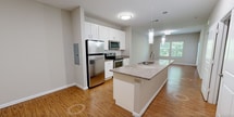 This well-appointed one-bedroom, one-bathroom residence in Durham, NC offers a thoughtfully designed single-floor layout with a comfortable, functional flow throughout. The open-concept living, dining, and kitchen area serves as the heart of the home, featuring warm hardwood-style flooring, neutral walls, and an abundance of natural light from multiple windows. The kitchen stands out with a large granite-topped island with an undermount sink, sleek white cabinetry, a subway tile backsplash, stainless steel appliances including a refrigerator, range, microwave, and dishwasher, and modern pendant lighting overhead. A door off the living area provides direct access to a private balcony. The bedroom is carpeted for comfort, includes a ceiling fan, and connects conveniently to the full bathroom, which features a granite vanity, white cabinetry, and hardwood-style flooring. Three closets offer generous storage throughout the unit. A dedicated laundry area with in-unit washer and dryer hookups, a utility room, and a welcoming entrance with louvered closet doors round out the space. Clean finishes and a neutral palette create a cohesive, move-in-ready environment.