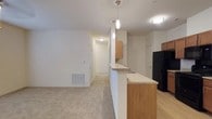This single-floor unit is thoughtfully designed with a practical, open layout that connects the kitchen and living areas seamlessly. The kitchen is well-equipped, featuring warm medium-toned wood cabinetry, granite-style countertops, and a full suite of black appliances including a refrigerator, electric range, built-in microwave, and dishwasher. Light hardwood-style flooring runs throughout the kitchen, which opens to a peninsula breakfast bar with pendant lighting overhead, providing a natural transition into the carpeted living and dining areas. The living room is generously proportioned, featuring a ceiling fan, a floor-to-ceiling door with adjacent window allowing natural light in, and direct access to an outdoor area.

The bedrooms are carpeted and comfortably sized, each with a window for natural light and ceiling fan fixtures. Closet storage is well-represented, including a walk-in closet in the primary bedroom and a built-in shelved closet in a secondary bedroom. The primary bathroom includes a soaking tub, hardwood-style flooring, and a wide granite-topped vanity. A second bathroom offers a single-sink vanity with matching granite countertops. The unit maintains a clean, neutral palette throughout.