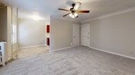 Located at 105 Ward Pkwy in Kansas City, Missouri, this one-bedroom, one-bathroom unit offers a well-organized single-floor layout. The main living area is carpeted and finished with classic crown molding along the ceiling, lending a touch of traditional character to the space. A ceiling fan with integrated lighting serves as a central fixture, providing both airflow and ambient illumination. Natural light filters in through windows fitted with blinds, and a wall-mounted air conditioning unit ensures year-round comfort. The kitchen area is positioned adjacent to the main living space and features warm-toned cabinetry, with tile flooring that distinguishes it from the carpeted rooms. The generously sized bedroom continues the carpeted aesthetic with crown molding, a ceiling fan, and windows that invite natural light. A dedicated closet provides storage off the bedroom. The bathroom is clean and functional, featuring a vanity with under-cabinet storage, a mirrored medicine cabinet, and tile flooring. The overall color palette is neutral and light throughout, with soft beige walls and white trim contributing to a bright, cohesive atmosphere. The layout makes efficient use of space, offering a practical and comfortable living environment in a well-known Kansas City neighborhood.