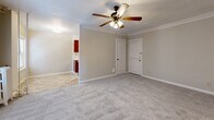 Located at 105 Ward Pkwy in Kansas City, Missouri, this one-bedroom, one-bathroom unit offers a well-organized single-floor layout. The main living area is carpeted and finished with classic crown molding along the ceiling, lending a touch of traditional character to the space. A ceiling fan with integrated lighting serves as a central fixture, providing both airflow and ambient illumination. Natural light filters in through windows fitted with blinds, and a wall-mounted air conditioning unit ensures year-round comfort. The kitchen area is positioned adjacent to the main living space and features warm-toned cabinetry, with tile flooring that distinguishes it from the carpeted rooms. The generously sized bedroom continues the carpeted aesthetic with crown molding, a ceiling fan, and windows that invite natural light. A dedicated closet provides storage off the bedroom. The bathroom is clean and functional, featuring a vanity with under-cabinet storage, a mirrored medicine cabinet, and tile flooring. The overall color palette is neutral and light throughout, with soft beige walls and white trim contributing to a bright, cohesive atmosphere. The layout makes efficient use of space, offering a practical and comfortable living environment in a well-known Kansas City neighborhood.