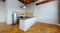 Located at 700 Stockton St in Richmond, Virginia, this single-floor loft residence showcases a compelling blend of industrial heritage and modern updates. The space retains much of its original character, with striking exposed brick walls, warm hardwood flooring throughout, and heavy timber beam construction visible across the ceilings — hallmarks of a thoughtfully preserved historic conversion.

The open main living area is anchored by tall arched windows that flood the interior with abundant natural light, framing views of the surrounding neighborhood. Exposed metal ductwork runs overhead, complementing the raw, industrial aesthetic of the space.

The kitchen is well-appointed with light wood cabinetry, dark granite countertops, and a full suite of stainless steel appliances, including a refrigerator, stove, and dishwasher. A peninsula-style counter extends into the living area, providing additional workspace and a natural division between cooking and living zones.

The bedrooms continue the loft's industrial character, featuring the same rich hardwood floors and exposed timber columns that give the space its distinctive personality. The bathroom offers a clean, updated contrast with white tile flooring, a single-vanity with white cabinetry, a combination tub and shower, and brushed nickel fixtures throughout. Together, these elements create a cohesive and characterful living environment rooted in Richmond's industrial history.