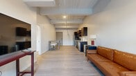 Located in the heart of downtown Wichita at 150 N Main St, this single-floor urban unit blends industrial character with modern finishes throughout its thoughtfully arranged layout. Exposed structural beams and ceiling details add architectural interest, while light wood-tone flooring flows consistently across all areas, creating a cohesive and clean aesthetic.

The open-plan living and dining area is generously proportioned, offering ample room for both relaxing and entertaining. Large windows in the living space provide natural light and frame views of a private outdoor patio, accessible via a stepped entryway — a notable feature that adds functional outdoor space to the unit. The kitchen is well-equipped with dark espresso cabinetry, granite-style countertops, a white tile backsplash, and a full suite of stainless steel appliances including a refrigerator, range, microwave, and dishwasher.

Two separate bedrooms each feature exposed beam ceilings and light-filled windows with blinds for privacy. The bathroom is finished with white cabinetry, granite countertops, and wood-look flooring. Throughout the unit, the design maintains a balanced urban-contemporary atmosphere suited to downtown living.