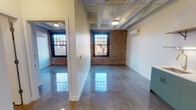 Located at 1515 W Monroe St in Chicago's vibrant West Loop neighborhood, this single-floor unit blends industrial character with contemporary finishes throughout. The space is defined by polished concrete floors that reflect light across every room, exposed structural beams overhead, and original brick walls that add warmth and texture to the interior.

The open living and main areas feature large, multi-pane windows set within the exposed brick walls, allowing generous natural light and neighborhood views to fill the space. A wall-mounted mini-split HVAC unit provides efficient climate control. The layout includes a distinct partition that separates the main living zone from an additional room, offering functional flexibility.

The kitchen is thoughtfully appointed with sage-green lower cabinetry, crisp white upper cabinets, open wood shelving with brass brackets, a stainless steel gas range, microwave, and a full-size stainless steel refrigerator — all set against a clean white tile backsplash.

A private room features exposed beam ceilings, polished floors, and access to a dedicated closet area. The bathroom includes a wood-toned vanity with a white countertop, a framed mirror, pendant lighting, and tiled shower walls, maintaining a clean, modern aesthetic consistent with the rest of the unit.