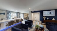 Located at 4010 Linkwood Dr in Houston, Texas, this single-story space showcases a thoughtfully designed interior that blends contemporary style with comfortable functionality. The open-concept layout connects a spacious lounge area, a dining zone, and a well-appointed kitchen, creating a seamless flow throughout.

The lounge area serves as the focal point of the space, anchored by a striking navy blue accent wall mounted with a large flat-screen display. Deep navy velvet club chairs are arranged atop a fluid, wave-patterned area rug, complemented by hexagonal tile flooring that transitions into warm wood tones. Decorative vases, sculptural accents, and potted greenery add character and depth to the room. Multiple windows fitted with blinds allow ample natural light to fill the space, while glass-panel doors provide additional brightness and outdoor access.

Adjacent to the lounge, a long white countertop workspace or bar area with seating extends toward the dining space, which features a dining table surrounded by upholstered chairs beneath bold geometric-patterned curtains.

The kitchen is finished to a high standard, featuring grey shaker-style cabinetry, quartz countertops, a shimmering tile backsplash, and stainless steel appliances including a French door refrigerator and dishwasher. Crystal pendant lights add an elegant finishing touch overhead.