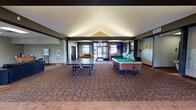 This single-floor community amenity building offers a comprehensive range of shared facilities designed to foster recreation, convenience, and social engagement. The main entrance opens into a generously sized common area with a vaulted ceiling and patterned carpeting, immediately establishing a welcoming atmosphere. This central hub houses both a ping-pong table and a full-size pool table, making it a natural gathering point for residents.

Adjacent to the game area is a comfortable lounge furnished with leather sofas and a large wall-mounted flat-screen television, with tile flooring and windows providing views of the surrounding outdoor greenery. The rental office is accessible near the entrance, flanked by seating for visitors.

The fitness center is well-equipped with cardio machines including treadmills and ellipticals, as well as a multi-station strength training unit, and benefits from natural light through a window overlooking the grounds.

A dedicated dining area features multiple tables and chairs with tile flooring and natural light. The building also includes a laundry room with multiple washers and dryers, and a mailbox area conveniently located near the main corridor, rounding out this full-service community facility.