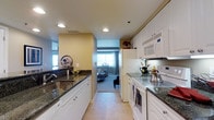 Located at 2145 Route 38 in Cherry Hill, New Jersey, this single-floor residence offers a thoughtfully designed layout that balances functionality and comfort. The galley-style kitchen serves as a central feature of the home, showcasing dark granite countertops that contrast elegantly with the crisp white cabinetry and white appliances, including a full-size refrigerator, electric range, and built-in microwave. Recessed lighting illuminates the kitchen, highlighting the clean lines of the space and the tile flooring underfoot. The kitchen flows directly into the living area, creating an open and connected feel between the two spaces. The living area is carpeted and benefits from natural light streaming in through a window, lending a warm and inviting ambiance to the room. Warm yellow-toned walls in the kitchen transition into cooler, neutral tones in the living space, adding visual interest throughout. The overall design reflects a practical yet comfortable living environment, well-suited for everyday living in the heart of Cherry Hill, a vibrant community in southern New Jersey.