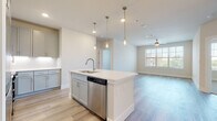 This well-designed single-floor residence showcases a clean, contemporary aesthetic throughout. The heart of the home is an open-concept kitchen and living area, where light wood-look flooring, crisp white walls, and abundant natural light create a bright and welcoming atmosphere. The kitchen is thoughtfully equipped with a central island featuring an integrated sink and stainless steel dishwasher, complemented by soft gray shaker-style cabinetry, white quartz countertops, a subway tile backsplash, and a full suite of stainless steel appliances including a range, microwave, and refrigerator. A trio of pendant lights adds a modern touch above the island. The adjacent living area features a ceiling fan and a window that fills the space with natural light. A built-in desk nook provides a convenient workspace off the main living area. The bedrooms are carpeted for comfort, each equipped with a ceiling fan and windows offering outside views. The primary bathroom offers a dual-sink vanity with gray cabinetry and gold-toned fixtures, a glass-enclosed shower, and wood-look flooring. A second bathroom mirrors the refined finishes, featuring a soaking tub with tiled surround. A generous walk-in closet with wire shelving completes the primary suite.
