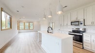 Located at 1115 Seigle Ave in Charlotte, NC, this single-floor space offers a thoughtfully designed open-concept layout with clean, contemporary finishes throughout. Light hardwood-style flooring runs continuously across the living areas, creating a cohesive and airy feel.

The kitchen serves as a central hub, featuring a large island with an undermount sink and matte black faucet, illuminated by three pendant cage-style lights overhead. White shaker cabinetry extends to the ceiling, offering generous storage, while a white subway tile backsplash and stainless steel appliances — including a range, microwave, and French door refrigerator — complete the modern aesthetic. The kitchen opens directly into a spacious living area bathed in natural light from multiple wood-framed windows overlooking lush greenery.

The bedrooms are bright and well-proportioned, with large windows and light-toned flooring. At least one bedroom includes a walk-in closet with built-in shelving. The bathrooms feature white shaker vanities with dark countertops, wood-framed mirrors, and tile-surround tub-shower combinations. A dedicated laundry room houses a full-size washer and dryer. The overall ambiance is clean, bright, and move-in ready.