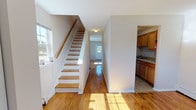 Located at 134 Ridgewood Ave in Pleasant Hills, NJ, this two-floor home offers a straightforward and functional layout spread across two levels. Warm hardwood flooring runs throughout the main living areas, reflecting natural light and lending a cohesive, classic character to the interior. The main floor features an open entryway with a staircase accented by a wood banister, leading into a central hallway that connects the key living spaces. The living area is generously proportioned, with large windows that invite abundant natural light and views of the surrounding greenery. Adjacent to the living space, the kitchen is efficiently arranged in a galley style, outfitted with warm wood cabinetry, granite-look countertops, a gas range, and a full-size refrigerator. Tile flooring grounds the kitchen area, providing a practical contrast to the hardwood in the rest of the home. A back door with a windowed panel offers additional access and light to the rear of the main floor. Upstairs, the bedrooms continue the hardwood flooring theme and feature multiple windows, baseboard heating, and wall-mounted air conditioning units for year-round comfort. The bathroom is clean and functional, with tile flooring, a full tub-shower combination, and a vanity with ample storage.