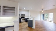 This two-floor, 1-bedroom, 1-bathroom townhouse-style unit offers a well-organized layout with the garage and entry on the lower level and the main living spaces above. The ground floor includes an attached garage with automatic opener, concrete flooring, and direct interior access via a carpeted staircase leading to the main level.

The upper floor hosts a bright, open-concept living, dining, and kitchen area finished with warm hardwood-style flooring throughout. The kitchen features two-tone cabinetry — white upper cabinets paired with dark lower cabinets — white quartz countertops, a peninsula with a sink, and a full suite of stainless steel appliances including a refrigerator, range, and over-the-range microwave. Recessed lighting illuminates the space. A pantry provides additional storage. The living and dining area is bathed in natural light, with sliding glass doors opening onto a private balcony overlooking a landscaped community with mature trees and neighboring homes.

The bedroom is a comfortable, light-filled room with a large window and hardwood-style flooring. The full bathroom includes a combined tub/shower, a dark-cabinetry vanity with white countertop, and hardwood-style flooring. Additional features include a dedicated laundry area, multiple closets, and two hallways connecting the spaces efficiently.