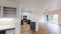 This two-floor, 1-bedroom, 1-bathroom townhouse-style unit offers a well-organized layout with the garage and entry on the lower level and the main living spaces above. The ground floor includes an attached garage with automatic opener, concrete flooring, and direct interior access via a carpeted staircase leading to the main level.

The upper floor hosts a bright, open-concept living, dining, and kitchen area finished with warm hardwood-style flooring throughout. The kitchen features two-tone cabinetry — white upper cabinets paired with dark lower cabinets — white quartz countertops, a peninsula with a sink, and a full suite of stainless steel appliances including a refrigerator, range, and over-the-range microwave. Recessed lighting illuminates the space. A pantry provides additional storage. The living and dining area is bathed in natural light, with sliding glass doors opening onto a private balcony overlooking a landscaped community with mature trees and neighboring homes.

The bedroom is a comfortable, light-filled room with a large window and hardwood-style flooring. The full bathroom includes a combined tub/shower, a dark-cabinetry vanity with white countertop, and hardwood-style flooring. Additional features include a dedicated laundry area, multiple closets, and two hallways connecting the spaces efficiently.