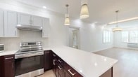 This well-appointed 2-bedroom, 2-bathroom residence in Milford, CT offers a thoughtfully designed single-floor layout with modern finishes throughout. Light hardwood flooring flows seamlessly from room to room, complemented by crisp white walls and recessed lighting that create a bright, clean aesthetic.

The kitchen is a standout feature, showcasing rich dark-wood cabinetry paired with white upper cabinets and a striking herringbone tile backsplash. A spacious peninsula with a quartz countertop and pendant lighting anchors the space, while a full suite of stainless steel appliances — including a refrigerator, range, dishwasher, and microwave — provides modern functionality. Crown molding adds a refined touch as the kitchen opens into the living area.

The primary bedroom is generously sized, featuring multiple windows with exterior views and a wall-mounted HVAC unit. The second bedroom is also well-proportioned with natural light from a window. Both bathrooms are elegantly finished, with one featuring marble-style tile flooring and walls, a sliding glass-enclosed shower, and white cabinetry. Multiple hallways and closets offer practical storage throughout. The overall ambiance is clean, modern, and move-in ready.
