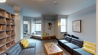 Located at 400 South Greene Street in Greenville, NC, this thoughtfully designed single-floor communal space blends contemporary aesthetics with functional versatility. The main lounge area features plush gray sectional sofas, accent chairs in bold blue and yellow, and a striking live-edge wood coffee table, all set against a neutral palette of soft grays and warm accent lighting. Built-in window benches with cushioned seating invite natural light from large windows, enhancing the welcoming atmosphere. A sculptural wood bookshelf serves as a natural room divider, anchoring the open-plan layout alongside a circular pendant light. The space includes a dedicated seating area lined with sleek black chairs, ideal for presentations or group gatherings, with a long marble-topped counter and neon signage as a dramatic focal point. A private meeting room offers a round table, ergonomic seating, a glass whiteboard, and bold artwork, providing a focused environment for small groups. Intimate booth seating areas feature dark leather banquettes, statement patterned wallcovering, and modern pendant lighting above marble-top tables. Curated artwork, including large-scale paintings and framed prints, is displayed throughout, contributing to the space's creative and professional character.