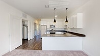 Located at 19 N Clinton Ave, Unit 208 in Bay Shore, NY, this single-floor residence offers a well-designed layout with modern finishes throughout. The open-concept kitchen is a standout feature, showcasing crisp white shaker cabinetry, dark quartz countertops, and a large central island topped with matching stone. Stainless steel appliances — including a refrigerator, range, and built-in microwave — provide full functionality, while two sleek black pendant lights add a contemporary touch overhead. Dark hardwood-style flooring anchors the kitchen and utility areas, creating a striking contrast with the white cabinetry. The bedrooms are finished with plush carpeting and feature large windows fitted with blinds, allowing for ample natural light and outdoor views. A ceiling fan is present in one bedroom for added comfort. Closet space includes wire-rack shelving for practical storage. The bathroom is appointed with light wood-look tile flooring, a white vanity with dark countertop, and a glass-enclosed walk-in shower with white subway tile surround and chrome fixtures. The overall aesthetic is clean, modern, and move-in ready, with a neutral palette that complements a variety of interior styles.