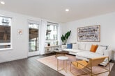 This single-floor residence offers a thoughtfully designed open-concept layout that balances modern aesthetics with everyday functionality. Rich dark hardwood flooring flows consistently throughout the space, tying each area together with a warm, cohesive feel.

The kitchen is a standout feature, outfitted with sleek two-tone cabinetry in a light grey and wood-grain finish, white quartz countertops, and a crisp subway tile backsplash. A full suite of stainless steel appliances — including a dishwasher, range, and built-in microwave — completes this well-equipped cooking space. Large windows allow natural light to pour in, brightening the room considerably.

The living area is open and inviting, anchored by large windows that bring in abundant natural light. The space is versatile, accommodating distinct lounging and seating zones, and features a ceiling fan for added comfort. A wide arched mirror serves as a striking design accent, adding depth and visual interest to the room.

A hallway connects the main living spaces to additional rooms, with recessed lighting overhead and clean white walls that contribute to the bright, airy atmosphere throughout.

The bathroom is clean and contemporary, featuring a wood-toned vanity with white countertop, a large mirror, and hardwood-style flooring consistent with the rest of the residence. Recessed lighting ensures the space is well-lit and functional.