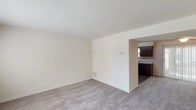 This two-floor space offers a practical and cohesive layout with neutral tones and functional finishes throughout. On the main level, the living area is finished with plush carpet and connects openly to the kitchen through a wide passageway. A ceiling fan with light fixture anchors the living space, which benefits from natural light via sliding glass patio doors dressed with vertical blinds, providing convenient outdoor access. The kitchen is well-equipped, featuring rich dark-stained cabinetry that extends to the upper walls, light granite-style countertops, and durable wood-look plank flooring. Black appliances — including a refrigerator, electric range with overhead ventilation, and dishwasher — are neatly integrated into the U-shaped layout. A window above the sink adds natural light to the workspace.

Upstairs, multiple bedrooms are carpeted and maintain the space's neutral palette. Each room includes windows that bring in natural light, and at least one bedroom features a dedicated closet with a hanging rod. The full bathroom includes a tub-shower combination with white subway tile surround, a single vanity with sink, and a large mirror. A staircase with decorative railing connects the two floors, completing this well-organized multi-level layout.