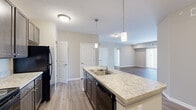Located at 4584 Samoyed Dr in Columbus, Ohio, this single-floor residence offers a thoughtfully designed open-concept layout finished with neutral tones and modern touches throughout. The kitchen serves as a central hub of the home, showcasing rich dark-stained cabinetry, light granite-style countertops, a central island with a double-basin sink, pendant lighting, and black appliances including a range, microwave, dishwasher, and refrigerator. The kitchen flows seamlessly into the living area, which features durable hardwood-style plank flooring, recessed lighting, and a large sliding glass door that invites abundant natural light and provides outdoor views. The bedroom is generously proportioned with plush carpet flooring, a walk-in closet equipped with multi-level wire shelving and hanging rods, and direct access to a private hallway. The bathroom is cleanly appointed with a granite-style vanity countertop, dark cabinetry, a large mirror, and a walk-in shower. Additional storage closets are visible throughout the unit. The overall ambiance is clean, contemporary, and move-in ready, with a cohesive neutral palette tying each space together.