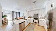 Located at 5300 N Mays St in Georgetown, TX, this thoughtfully designed one-bedroom, one-bathroom residence offers a bright and contemporary living experience across a single floor. The open-concept layout seamlessly connects the kitchen and living room, creating an inviting, airy atmosphere bathed in natural light from large windows dressed with elegant gray curtains.

The kitchen is a standout feature, showcasing crisp white shaker cabinetry with matte black hardware, quartz countertops, a subway-tile backsplash, and a full suite of stainless steel appliances including a refrigerator, range, microwave, and dishwasher. A peninsula with seating provides additional prep space and casual dining. Light wood-style flooring runs throughout, tying the spaces together cohesively.

The living area offers a comfortable retreat with recessed lighting and room for relaxed seating arrangements. The bedroom is a serene space featuring a window with natural light and direct access to the well-appointed bathroom. The bathroom includes a soaking tub and shower combination, a single vanity with white cabinetry, and clean tile finishes. A dedicated walk-in closet with built-in shelving and hanging rods provides practical storage, completing this efficiently designed and modern residence.