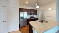 This single-floor residence offers a thoughtfully designed layout with modern finishes and a cohesive aesthetic throughout. The open-concept kitchen serves as a central highlight, showcasing rich dark-espresso cabinetry, granite countertops, a tile backsplash, and a full suite of stainless steel appliances including a gas range, built-in microwave, and French door refrigerator. A peninsula with an undermount sink and pendant lighting above provides additional prep space and connects seamlessly to the living area, which features neutral carpet, soft warm-toned walls, and access to an exterior door with adjacent windows that invite natural light.

The bedrooms are generously sized, each carpeted and equipped with windows offering outdoor views. One bedroom connects directly to a walk-in closet featuring white wire shelving along two walls, providing ample storage capacity. The bathrooms include a full bath with a tub-shower combo, wood-look flooring, and a vanity with granite countertops and dark cabinetry, while a secondary bathroom features a stand-up shower and access to an additional closet. The overall ambiance is clean, contemporary, and move-in ready.