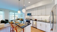 This thoughtfully designed one-bedroom, one-bathroom residence maximizes every square foot through a clean, modern layout and cohesive contemporary finishes throughout. The open-concept kitchen is a standout feature, showcasing crisp white shaker cabinetry extending to the ceiling, a classic subway tile backsplash, dark countertops, and a full suite of stainless steel appliances including a gas range and dishwasher. A central island with seating and globe pendant lighting above adds both functionality and style, flowing seamlessly into the dining and living areas. The living room is bright and airy, benefiting from large windows with outdoor views that flood the space with natural light. Warm hardwood-style flooring runs throughout the main living areas, tying the open plan together. The bedroom is a serene retreat, featuring a window with outdoor views, soft neutral tones, and a walk-in closet offering generous storage. The bathroom is finished with white subway tile in a glass-enclosed shower, marble-style flooring, and polished chrome fixtures, creating a clean, spa-like atmosphere. Hallways connect each area efficiently, maintaining a sense of flow throughout the home. Overall, the space presents a refined, modern ambiance ideal for comfortable single-occupancy living.