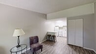 This single-story, one-bedroom, one-bathroom unit offers a thoughtfully arranged floor plan that maximizes its compact footprint. Warm hardwood-style flooring runs throughout the space, creating a cohesive and inviting atmosphere from room to room.

The living area is bright and open, featuring a ceiling fan with a light fixture and a textured ceiling. A large window allows natural light to fill the room while providing an outdoor view, and a wall-mounted heating unit sits beneath it. The living area flows directly into the kitchen, which is designed with white shaker-style cabinetry extending to the ceiling, granite-look countertops, and a peninsula that adds additional prep and dining space. White appliances include a range, dishwasher, and refrigerator, complemented by an overhead exhaust hood.

The bedroom is a comfortable size, featuring a wide louvered bi-fold closet, a ceiling fan, natural light from a window, and crown molding details. The full bathroom includes a combined tub and shower, a vanity with an integrated sink, and a large mirror. A dedicated utility room and hallway with a louvered closet door complete the layout.