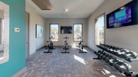 Located at 801 Del Rio Pike in Franklin, Tennessee, this well-appointed fitness center offers a comprehensive, single-floor workout facility designed to support a wide range of exercise routines. The space is organized into distinct functional zones, each thoughtfully equipped to meet varied fitness needs.

The cardio area features a lineup of True-brand treadmills, an elliptical trainer, and a rowing machine, each positioned beneath wall-mounted flat-screen televisions for entertainment during workouts. Multiple windows along the walls flood this zone with natural light while providing views of the surrounding outdoor areas.

Adjacent to the cardio section, a dedicated cycling studio houses several stationary spin bikes arranged facing a central mounted television, creating an immersive indoor cycling experience. A dumbbell rack with a full range of free weights is also conveniently positioned nearby.

A separate flexibility and functional training area is distinguished by a vibrant teal accent wall and ceiling fan, contributing to a bright, energizing atmosphere. This zone is stocked with stability balls in multiple sizes, resistance equipment, yoga mats, and a True-brand stretch/pilates machine, offering ample options for low-impact and recovery-focused training.

Throughout the facility, neutral gray carpet tiles, recessed lighting, and contemporary abstract wall art create a clean, modern aesthetic that is both motivating and welcoming.