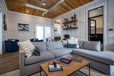 Located at 300 S Tulane Ave in Oak Ridge, Tennessee, this thoughtfully designed single-floor clubhouse serves as a welcoming community hub with a refined yet relaxed aesthetic. Warm knotty pine tongue-and-groove ceilings span the main gathering areas, complementing light hardwood flooring and crisp white wainscoting and panel molding throughout.

The central lounge area anchors the space with a comfortable sectional sofa, a herringbone-patterned feature wall, a mounted fireplace, and a wall-mounted TV—creating an inviting setting for relaxation or socializing. Adjacent to it, a seating nook outfitted with plush navy swivel chairs and a round table is separated by frosted glass sliding doors, offering a quieter retreat.

The kitchenette area is well-appointed with granite countertops, a stainless steel side-by-side refrigerator, microwave, and a stylish tile backsplash. A cafe-style seating zone with bar-height tables and chairs lines a wainscoted wall nearby, ideal for casual gatherings. Large windows flood this area with natural light and frame views of the surrounding outdoor greenery.

A dedicated workstation with a desk and computer provides a functional workspace, while a separate mail and package room features rows of secure mailboxes and parcel lockers. Together, these amenities create a polished, community-centered environment designed for both productivity and leisure.