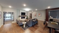 Located at 2180 Highway 13 in Mendota Heights, MN, this single-floor community space offers a thoughtfully designed interior that blends contemporary style with comfortable, functional living. Warm hardwood flooring flows seamlessly throughout, unifying the various seating and gathering areas into a cohesive, inviting environment.

The main lounge area serves as the focal point of the space, anchored by a sleek linear gas fireplace set within a white-painted brick surround and topped with a rich wood mantel. A wall-mounted flat-screen television above the fireplace makes this a natural gathering spot, while mid-century modern armchairs and a plush sectional sofa arranged around area rugs provide ample seating for relaxation and socializing.

Adjacent to the lounge, a generously sized dining area features a dark wood table with coordinating chairs, bathed in natural light from large windows that offer views of the surrounding greenery. A cozy banquette nook with deep burgundy upholstery and bistro-style seating adds an intimate dining option nearby.

The entry area is accented by curated abstract artwork, lush potted plants, and recessed lighting, creating a welcoming transition into the space. Glass-paneled doors add a touch of architectural sophistication while maintaining visual openness. Overall, the space exudes a modern, polished ambiance ideal for community gatherings and everyday use.