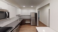 This single-floor unit offers a thoughtfully designed layout with a clean, contemporary aesthetic throughout. The kitchen is a standout feature, equipped with stainless steel appliances including a range, microwave, dishwasher, and refrigerator, complemented by crisp white upper cabinetry, dark wood lower cabinets, gray countertops, and a classic white subway tile backsplash. Recessed lighting illuminates the space efficiently, while light hardwood-style flooring adds warmth and continuity into the adjacent living and dining areas. A walk-in closet with built-in wire shelving provides generous storage directly off the main living space. The living area is open and airy, featuring natural light from windows and a wall-mounted HVAC unit for year-round comfort, along with baseboard heating. The bedrooms are finished with plush carpeting, ceiling fans with integrated lighting, and windows with blinds that allow for adjustable natural light. Each bedroom also includes baseboard heating. The bathroom presents a modern, accessible design with large-format dark tile flooring, a walk-in tiled shower with a handheld fixture, a floating vanity with a white sink, mirrored medicine cabinet, and chrome grab bars for added safety and convenience.