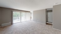 This single-floor unit offers a practical and cohesive layout designed for comfortable everyday living. The open living area is finished with neutral-toned carpet and painted in warm gray tones, creating a calm, understated ambiance throughout. A large sliding glass door fitted with vertical blinds fills the space with natural light and provides direct access to a balcony overlooking mature trees, adding a pleasant outdoor connection.

The kitchen is outfitted with crisp white cabinetry, brushed nickel hardware, and a generous granite countertop featuring speckled gray and white tones. A double stainless steel undermount sink with a gooseneck faucet serves as the functional centerpiece, complemented by ample upper and lower cabinet storage.

The bedrooms continue the neutral carpet and gray wall palette, each receiving natural light through windows dressed with vertical blinds. One bedroom includes a built-in closet with bifold doors, offering organized storage. A second carpeted bedroom provides similar proportions and window placement.

The bathroom features a granite-topped vanity with a framed mirror, white cabinetry, and wood-look flooring. A full shower-tub combination and standard toilet complete the space, maintaining a clean and consistent finish throughout the unit.