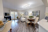 Located at 2551 Cornelia Rd in Herndon, Virginia, this well-appointed one-bedroom, one-bathroom residence offers a thoughtfully designed single-level layout. The open-concept main living area seamlessly connects the living room, dining room, and kitchen, creating an inviting and functional space bathed in natural light. Warm gray hardwood-style flooring runs throughout, complementing the neutral wall tones.

The kitchen is outfitted with stainless steel appliances — including a gas range, microwave, and refrigerator — white shaker cabinetry, a mosaic tile backsplash, and a quartz-style countertop. The living room features French doors that open to a private balcony, allowing abundant natural light and outdoor access. A wall-mounted TV area and open seating arrangement make the living space equally comfortable and practical.

The bedroom offers plush carpeting, large windows with natural light, and access to a generously sized walk-in closet with built-in shelving. Two additional closets provide ample storage throughout the unit. The full bathroom includes a soaking tub and shower combination, a wide vanity with a large mirror, and hardwood-style flooring. The overall aesthetic is clean, modern, and move-in ready.