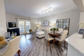 Located at 2551 Cornelia Rd in Herndon, Virginia, this well-appointed one-bedroom, one-bathroom residence offers a thoughtfully designed single-level layout. The open-concept main living area seamlessly connects the living room, dining room, and kitchen, creating an inviting and functional space bathed in natural light. Warm gray hardwood-style flooring runs throughout, complementing the neutral wall tones.

The kitchen is outfitted with stainless steel appliances — including a gas range, microwave, and refrigerator — white shaker cabinetry, a mosaic tile backsplash, and a quartz-style countertop. The living room features French doors that open to a private balcony, allowing abundant natural light and outdoor access. A wall-mounted TV area and open seating arrangement make the living space equally comfortable and practical.

The bedroom offers plush carpeting, large windows with natural light, and access to a generously sized walk-in closet with built-in shelving. Two additional closets provide ample storage throughout the unit. The full bathroom includes a soaking tub and shower combination, a wide vanity with a large mirror, and hardwood-style flooring. The overall aesthetic is clean, modern, and move-in ready.
