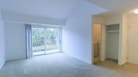 This two-floor space offers a clean, neutral interior designed for comfortable living. The upper level showcases a spacious, light-filled living area with vaulted ceilings that add a sense of openness and volume. Large sliding glass doors lead to a private balcony overlooking lush, tree-lined greenery, allowing abundant natural light to fill the room. Soft, neutral carpeting extends throughout the living area, contributing to a warm and inviting ambiance. A ceiling fan provides additional comfort overhead.

Adjacent to the living area, a dedicated laundry space with an in-unit washer is conveniently accessible behind a closet door. The lower level features a generously sized carpeted room, which opens to a bathroom equipped with warm wood-toned cabinetry and a vanity, visible through a connecting doorway.

The kitchen is efficiently laid out with wood-trimmed cabinetry, light countertops, a stainless steel sink, a dishwasher, and a full-size refrigerator. Light tile flooring and upper wall-mounted cabinets maximize storage and practicality. Throughout, the space maintains a consistent neutral palette, offering a versatile and move-in-ready environment.