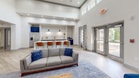 Located at 1533 Ellis Rd in Durham, NC, this well-appointed single-floor amenity facility offers a thoughtfully designed layout across a generous footprint. The grand living area immediately impresses with soaring double-height ceilings, striking sputnik-style chandeliers, and light wood-look flooring that flows throughout. A built-in kitchen bar with bold navy cabinetry, white subway tile backsplash, and bar seating serves as a stylish social hub, complemented by comfortable lounge seating and an open, airy atmosphere filled with natural light from large windows. The game room provides a dedicated recreation space, featuring a full-size pool table, wall-mounted TV, shiplap accent wall, and cozy lounge chairs with contemporary art pieces adorning the walls. A secondary lounge area offers additional seating, a fireplace, wall-mounted TV, and bistro-style table, ideal for casual gatherings. The expansive fitness center is a standout feature, housing a comprehensive array of cardio equipment including treadmills, ellipticals, and stationary bikes, alongside a full selection of strength and cable machines. Patterned carpet tiles, ceiling fans, and natural light from exterior windows create an energizing workout environment. An office and multiple connecting hallways complete the layout, ensuring smooth circulation throughout the space.