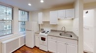 This single-floor unit offers a well-organized layout that maximizes its compact footprint. The kitchen is efficiently designed, featuring white cabinetry, granite-style countertops, a coil-burner range, a full-size refrigerator, and a stainless steel sink. Recessed lighting illuminates the space, while windows overlooking the surrounding brick building exterior allow natural light to filter in. A radiator unit beneath the windows provides heating.

The main living area is open and versatile, with warm hardwood flooring that extends throughout the unit. Multiple recessed ceiling lights brighten the room evenly. A built-in closet with a hanging rod provides convenient storage, and additional doorways offer access to adjoining spaces.

The bathroom maintains a clean, classic aesthetic with crisp white walls, a pedestal-style sink, a toilet, and a shower. The standout feature is the black-and-white mosaic tile flooring, adding a timeless design detail. A wall-mounted mirror and recessed lighting complete the space. Overall, the unit presents a neutral, move-in-ready environment with consistent finishes across all areas.