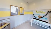This single-floor pet grooming and pampering station is thoughtfully designed with both functionality and charm in mind. The space is immediately recognizable by its distinctive tri-color wall treatment — soft light blue on the lower half, a bold yellow stripe in the middle, and white above — creating a bright and welcoming atmosphere for pets and their owners alike.

The room is equipped with a dedicated pet washing tub, ideal for bathing dogs of various sizes, along with a "Lather Up Pet Pampering Station" unit that provides grooming supplies and amenities. A stainless steel utility sink and cabinet offer practical washing and storage solutions. The durable, easy-to-clean flooring throughout is well-suited for a high-use grooming environment.

Natural light filters in through a glass-paneled exterior door and a window fitted with blinds, lending the space an open and airy feel. Decorative dog-themed artwork, including framed prints of dogs in a modern graphic style and wall-mounted dog head sculptures, add personality and reinforce the pet-friendly character of the space.

The overall ambiance is clean, organized, and purpose-built, making this pet station a convenient and enjoyable amenity for residents and their four-legged companions.