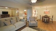 Located at 500 Avalon Way in Brandon, Mississippi, this single-story residence offers a welcoming and well-appointed interior designed for comfortable everyday living. The living area serves as the heart of the home, featuring rich hardwood-style flooring, warm neutral wall tones, and tasteful furnishings that create an inviting atmosphere. A ceiling fan with a light fixture provides both comfort and illumination, while a decorative mirror adds depth and character to the space. The living room flows naturally into the dining area, which is anchored by a classic wooden dining table and chairs, making the layout ideal for both casual meals and entertaining. A white console table with elegant detailing provides additional surface space and storage. An adjacent bathroom is visible from the living area, offering convenient access and featuring warm lighting and classic cabinetry. The consistent use of neutral tones, warm lighting, and cohesive decor throughout the space creates a unified and harmonious ambiance. The open sightlines between rooms enhance the overall sense of space and connectivity, making this single-floor home feel both functional and refined.
