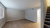 This two-story home offers a clean, modern aesthetic throughout, with thoughtfully updated finishes across both levels. The main floor features light wood-look luxury vinyl plank flooring that flows through the open living areas, complemented by neutral gray-toned walls and crisp white baseboards. A staircase with a black metal railing connects the two levels, adding a contemporary touch to the interior design.

The kitchen is outfitted with white shaker-style cabinetry, light marble-pattern countertops, and stainless steel appliances including an electric range and over-the-range microwave. A black matte faucet and matching cabinet hardware provide cohesive, modern detailing throughout.

The main floor also includes a half bathroom featuring wood-look tile flooring, a white vanity, and stylish black fixture accents including a round mirror and towel ring. A second full bathroom on the upper level mirrors this refined aesthetic with matching finishes.

The bedrooms are located on the upper floor, each carpeted in a soft gray tone and equipped with ceiling fans for added comfort. Windows with horizontal blinds allow natural light to fill these rooms. Additional rooms on the main level feature wood-look flooring in varying tones, offering flexible living and dining configurations. Textured ceilings and consistent neutral wall colors tie the entire home together with a cohesive, move-in-ready feel.