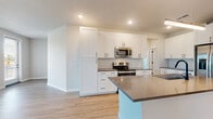Located at 4631 Whitfield Ave in Sarasota, Florida, this single-story home presents a clean, modern aesthetic throughout. The heart of the home is a well-appointed kitchen featuring crisp white shaker cabinetry, dark hardware accents, a vertical tile backsplash, and dark countertops. Stainless steel appliances — including a range, microwave, and refrigerator — complement the sleek design. A central island with a built-in sink and pendant lighting above adds both functionality and style, flowing naturally into the open living area. The living room is bright and airy, with light wood-look flooring, a ceiling fan, and multiple windows that invite natural light and outdoor views. Bedrooms are finished with plush carpeting, ceiling fans, and ample natural light from well-placed windows. A walk-in closet with wire shelving provides generous storage. The bathroom features large-format white wall tile in the tub/shower surround, complemented by matte black fixtures and fittings for a contemporary touch. A dedicated laundry room accommodates a full-size washer and dryer with additional wire shelving overhead. Throughout the home, light wood-look flooring, neutral wall tones, and matte black hardware create a cohesive, modern living environment.