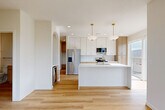 Located at 504 N 187th Ct in Elkhorn, Nebraska, this well-appointed 2-bedroom, 2-bathroom single-floor home showcases a clean, contemporary design with high-quality finishes throughout. The open-concept kitchen and living area serves as the heart of the home, anchored by a large center island with a white quartz countertop, gold-accented fixtures, and a deep undermount sink. Two pendant lights with brass hardware hang above the island, while stainless steel appliances, two-tone cabinetry combining white upper cabinets with natural wood lower cabinets, and light hardwood flooring complete the modern aesthetic. A large window and sliding glass door flood the space with natural light and provide outdoor views. The primary bedroom is generously sized, featuring hardwood floors, expansive windows overlooking a lush natural landscape, and an ensuite bathroom with a walk-in closet. The bathrooms are finished with warm wood vanities, gold hardware, sliding glass tub-shower enclosures, and light hardwood flooring. The secondary bedroom offers plush carpet, a ceiling fan, and windows with neighborhood views. Throughout the home, a neutral color palette, recessed lighting, and consistent gold accents create a cohesive, modern atmosphere.