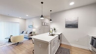 This well-designed one-bedroom, one-bathroom unit at 700 N 40th St in Rogers, Arkansas offers a thoughtfully planned single-floor layout with modern finishes throughout. The open-concept kitchen and living area serves as the heart of the home, featuring white shaker cabinets, a white quartz countertop island with an undermount sink, stainless steel appliances including a refrigerator, range, and microwave, and a subway tile backsplash. Stylish pendant lights hang above the island, which also provides bar seating for casual dining. The living area flows naturally from the kitchen, offering recessed lighting, warm wood-look flooring, and a large sliding glass door fitted with vertical blinds that allows natural light to fill the space. The bedroom is a comfortable retreat with a ceiling fan, a window with blinds, and the same warm flooring found throughout. It connects to a spacious walk-in closet outfitted with multi-level wire shelving for generous storage. The full bathroom features a tub-shower combination, a white vanity with quartz countertop, and wood-look flooring that ties into the rest of the unit. Neutral gray tones and clean white trim create a cohesive, contemporary aesthetic throughout.
