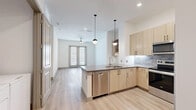 Located at 7777 Manderville Ln in Dallas, TX, this well-appointed one-bedroom, one-bathroom residence offers a thoughtfully designed open-concept layout. Light wood-tone flooring flows throughout, complementing the clean, neutral palette that defines the space.

The kitchen is a standout feature, showcasing light wood cabinetry with matte black hardware, a stone tile backsplash, and a full suite of stainless steel appliances including a refrigerator, range, microwave, and dishwasher. A central island with a dark countertop and pendant globe lighting above serves as both a prep area and casual gathering space. A built-in desk nook adds functional versatility adjacent to the kitchen.

The living area is bright and open, anchored by French doors that invite natural light and provide outdoor access. A ceiling fan overhead adds comfort to the space.

The bedroom is a calm, neutral retreat with light wood flooring and ample wall space. It connects to a generously sized walk-in closet equipped with multi-tier wire shelving for organized storage.

The bathroom features marble-look tile flooring, light wood cabinetry with a wide vanity and large mirror, and a full soaking tub. The overall design is modern, cohesive, and move-in ready.