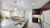 Located at 9950 Estero Oaks Dr in Fort Myers, FL, this single-floor residence offers a thoughtfully designed 2-bedroom, 2-bathroom layout that makes efficient use of its space. The open-concept kitchen flows seamlessly into the living and dining areas, anchored by a large granite-topped island with a double stainless steel sink and elegant pendant lighting overhead. Rich dark-espresso cabinetry lines the kitchen walls, complemented by stainless steel appliances including a refrigerator, range, and built-in microwave. Light wood-style flooring runs throughout, lending warmth and continuity to the interior. The living room is bright and inviting, featuring a ceiling fan and sliding glass doors that open to a private balcony overlooking a lush green landscape. Both bedrooms are comfortably sized, with the primary bedroom offering ample room, natural light from windows, and access to closet space. The second bedroom is equally well-lit with a ceiling fan and a serene, neutral palette. Each bathroom is finished with tile surround tub-shower combinations and clean, classic fixtures. A connecting hallway and two closets round out the functional layout, making this a practical and comfortable home in a Florida community setting.