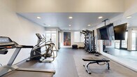 Located at 757 N Grant St in Denver, Colorado, this fitness center offers a thoughtfully designed exercise space across a single floor. The room features a clean, modern aesthetic with white walls, recessed lighting, and durable dark tile and rubber flooring that together create a functional yet polished atmosphere.

The space is well-appointed with a comprehensive selection of equipment to support a wide range of workout routines. Cardio options include a treadmill, elliptical, and stationary bike, while strength training is served by a multi-functional cable machine, adjustable weight bench, and selectorized machines. A full dumbbell rack stocked with hex weights, kettlebells, medicine balls, resistance bands, and barbell plates rounds out the free weights section, offering versatility for users at all fitness levels.

Large floor-to-ceiling glass doors and windows along one wall allow abundant natural light to fill the room and provide views toward the surrounding Denver neighborhood, creating an inviting and energizing environment. A wall-mounted flat-screen TV and a large mirror further enhance the space, making workouts both entertaining and easy to monitor. A vibrant abstract painting adds a touch of artistic character to the interior. The overall layout is open and spacious, allowing for comfortable movement between equipment stations.