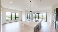 Located at 531 Laketower Drive in Lexington, Kentucky, this modern 2-bedroom, 2-bathroom residence offers a thoughtfully designed open-concept layout with high-end finishes throughout. The combined kitchen and living area serves as the heart of the home, anchored by a generous island with a sleek quartz countertop, undermount sink, and matte black pendant lighting. The kitchen features gray shaker cabinetry, white subway tile backsplash, and stainless steel appliances, all flowing seamlessly into the bright living area. Large black-framed windows and a wide sliding glass door flood the space with natural light and open to a private balcony with sweeping treetop and lake views. Light-toned hardwood flooring runs throughout the main living areas, adding warmth to the contemporary aesthetic. The primary bedroom is generously sized, featuring expansive windows with lake views and direct access to the en-suite bathroom, which includes a dual-sink white vanity with quartz counters, tile flooring, and a frameless glass walk-in shower. The second bedroom offers plush carpet, a large picture window with lake views, and convenient access to the main hall. Three closets, including a walk-in with wire shelving, provide ample storage. Clean white walls, panel-style doors with matte black hardware, and recessed lighting complete the refined, modern character of this well-appointed residence.
