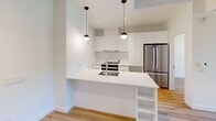 Located at 6085 Rue Sherbrooke Est in Montréal, this thoughtfully designed 2-bedroom, 2-bathroom unit offers a clean, contemporary aesthetic throughout its single-floor layout. Light hardwood flooring runs through the main living areas and bedrooms, lending warmth to the crisp white walls and modern finishes.

The kitchen is a standout feature, showcasing flat-front white cabinetry, stainless steel appliances including a French door refrigerator and range, and a large central island with a white quartz countertop, undermount sink, and built-in shelving. Stylish pendant lights hang above the island, adding a refined touch to the space.

Both bedrooms are bright and well-proportioned, benefiting from large windows that frame views of the surrounding greenery. The primary bedroom includes a dedicated closet, while the second bedroom also features its own closet and access to the hallway. Natural light fills each room, creating an airy, comfortable atmosphere.

The two bathrooms are finished in a consistent modern style, featuring large-format grey tile flooring, floating wood-toned vanities with white countertops, and generous mirrors. One bathroom includes a soaking tub with a glass shower enclosure. The unit is completed by a welcoming hallway entry, making for a practical and polished living space.