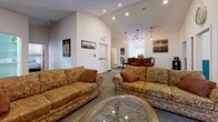 This penthouse-level space in Port Clinton, Ohio, offers a well-appointed single-floor layout with three bedrooms, three bathrooms, a hallway, and a fully equipped commercial kitchen. The interior carries a consistent nautical theme throughout, with teal accent walls, wood trim wainscoting, and coastal artwork providing a cohesive decorative identity.

The common living area features carpet flooring, recessed lighting, vaulted ceilings, and comfortable seating arranged around a central coffee table. Framed harbor and lighthouse artwork reinforces the waterfront character of the space. An adjacent dining area with pendant lighting adds a refined touch.

Each bedroom continues the teal-and-neutral color scheme. The spacious primary bedroom includes a ceiling fan, vaulted ceiling, multiple windows for natural light, and a fireplace with mounted TV. Additional bedrooms offer ceiling fans, bistro-style seating areas, and ample natural light through large windows.

The bathrooms are functionally designed with tiled flooring, walk-in showers, accessibility grab bars, and wood-toned vanities. The commercial kitchen is fully outfitted with stainless steel prep tables, professional-grade range with hood, and ample storage, supporting large-group use efficiently.