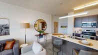 Located on West Broad Street in Richmond, Virginia, this contemporary single-floor residence offers a well-designed open-concept layout that seamlessly connects the living, dining, and kitchen areas. The space features polished concrete flooring throughout, contributing to a sleek, modern aesthetic complemented by neutral white walls and abundant natural light from multiple windows.

The kitchen is equipped with dark cabinetry, stainless steel appliances including a refrigerator, electric range, and microwave, along with a curved island featuring a light quartz countertop and bar seating — ideal for casual dining or entertaining. A pendant light above the island adds a refined touch.

The living area is bright and inviting, with a ceiling fan, large windows with sheer curtains, and ample space for comfortable seating arrangements. It flows naturally from the kitchen, creating a cohesive and functional common area.

The bedroom is well-lit by corner windows that offer outdoor views of the surrounding neighborhood, and it connects directly to a full bathroom featuring a single-sink vanity with quartz countertop, dark cabinetry, and a shower-tub combination. A spacious walk-in closet with built-in shelving and a natural light-admitting window provides generous storage. The overall ambiance is clean, contemporary, and functional.