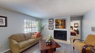 This single-story one-bedroom, one-bathroom residence in Memphis, Tennessee offers a thoughtfully designed layout with a range of functional features throughout. The living room serves as the central gathering space, finished with wood-style hard-surface flooring and anchored by a tile-surround fireplace with a sleek black face. A large window allows natural light to fill the room, creating a bright and welcoming atmosphere. Adjacent to the living area, a dedicated dining space provides an intimate setting for meals, with access connecting to the nearby kitchen. The galley-style kitchen is equipped with white cabinetry, marble-pattern countertops, a double-basin sink, and black appliances including a range, dishwasher, and refrigerator. A separate laundry closet with built-in shelving is conveniently tucked off the kitchen. The bedroom features plush carpet, a ceiling fan, a walk-in closet, and sliding glass doors opening to a private outdoor patio. The full bathroom includes a wide vanity with marble-pattern countertops, white cabinetry, a large mirror, and a shower-tub combination. Neutral gray walls and consistent finishes tie the space together throughout.